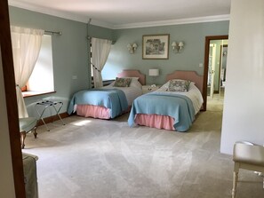 A bedroom with two beds, a window with curtains, a bedside table with a lamp, and a picture on the wall.