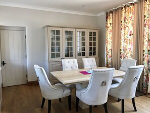 A dining area with a wooden table and four upholstered chairs, a cabinet with glass doors, and a door.
