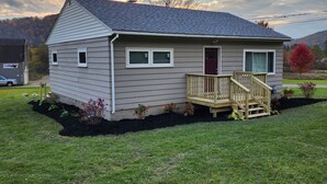 Ein Bungalow mit Veranda, einer roten Tür und einem kleinen Vorgarten mit Pflanzen.