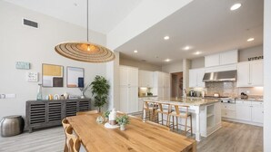 A modern kitchen with white cabinets, a central island, and a dining area with a wooden table and chairs.
