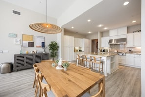 A modern kitchen with white cabinets, a central island, and a dining area with a wooden table and chairs. - PGA West Getaway with Pool & Fire Pit (La Quinta)