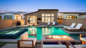 A swimming pool with lounge chairs and a fire pit, surrounded by a brick wall and a building with large windows. - PGA West Getaway with Pool & Fire Pit (La Quinta)