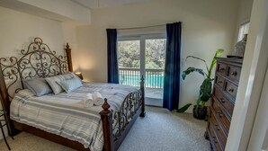 Een slaapkamer met een bed, een dressoir, een raam met gordijnen en een kamerplant.
