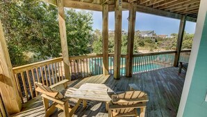 Een houten terras met twee Adirondack-stoelen en een tafel, met uitzicht op een zwembad en een strand.