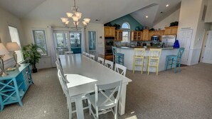 Een ruime keuken met een centraal eiland, houten kastjes en een grote eettafel met stoelen.
