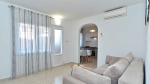 A modern living room with a beige sofa, a dining table with chairs, and a kitchen visible through an archway. - Holiday apartment with air conditioning (Bale)