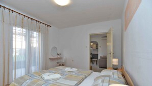 A hotel room with two beds, a bedside table with a lamp, a chair, a mirror, and a view of the hallway. - Holiday apartment with air conditioning (Bale)