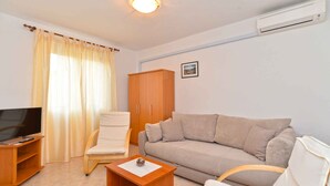 A living room with a television, sofa, armchair, wooden cabinet, and a small table.