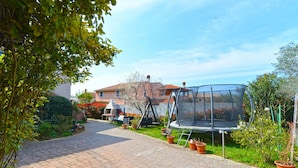 A paved garden path leading to a trampoline in a residential area with potted plants and a house in the background.
