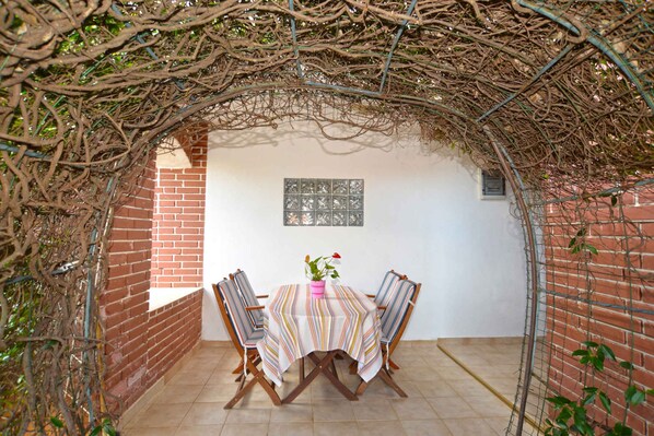 An outdoor dining area with a brick wall, a tiled floor, and a table with striped tablecloths and chairs.