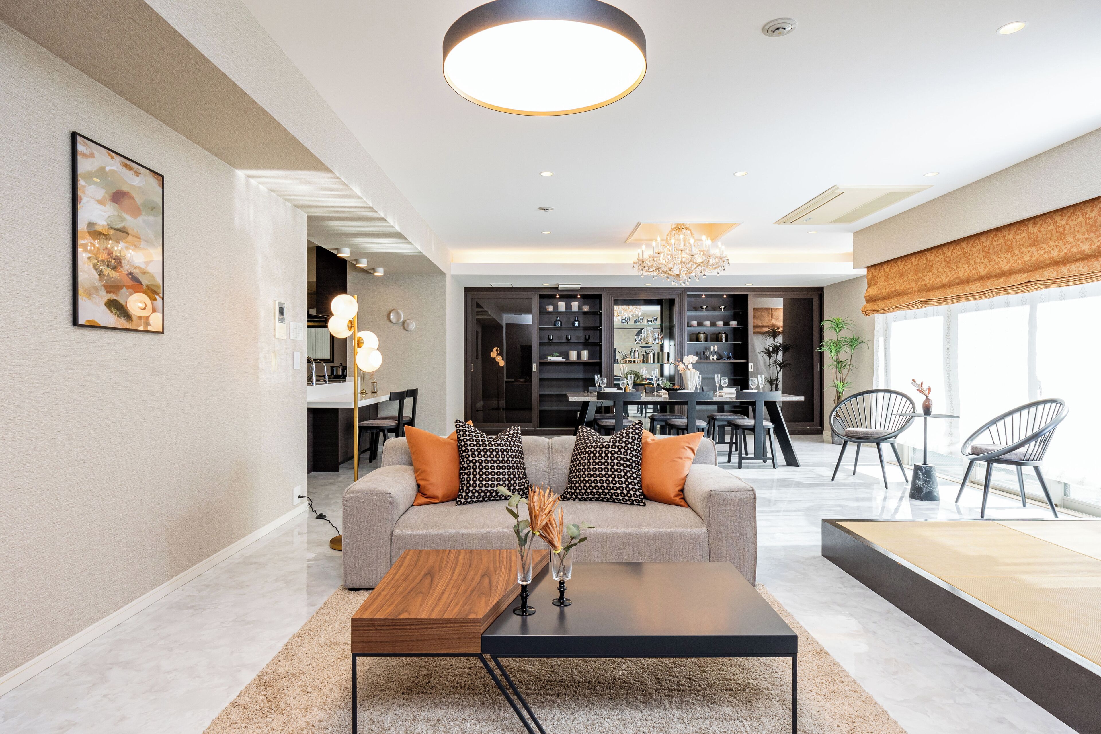 A modern living room with a sofa, coffee table, and chairs. There is a dining area with a table and chairs in the background.