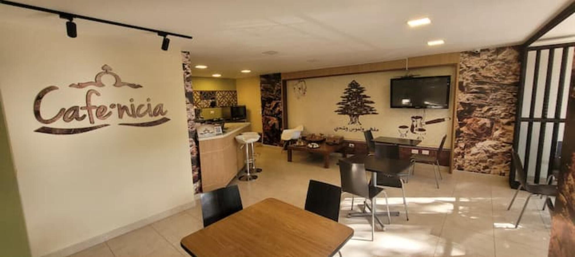 A dining area with a wooden table and chairs, a TV mounted on the wall, and a stone wall with a tree mural.