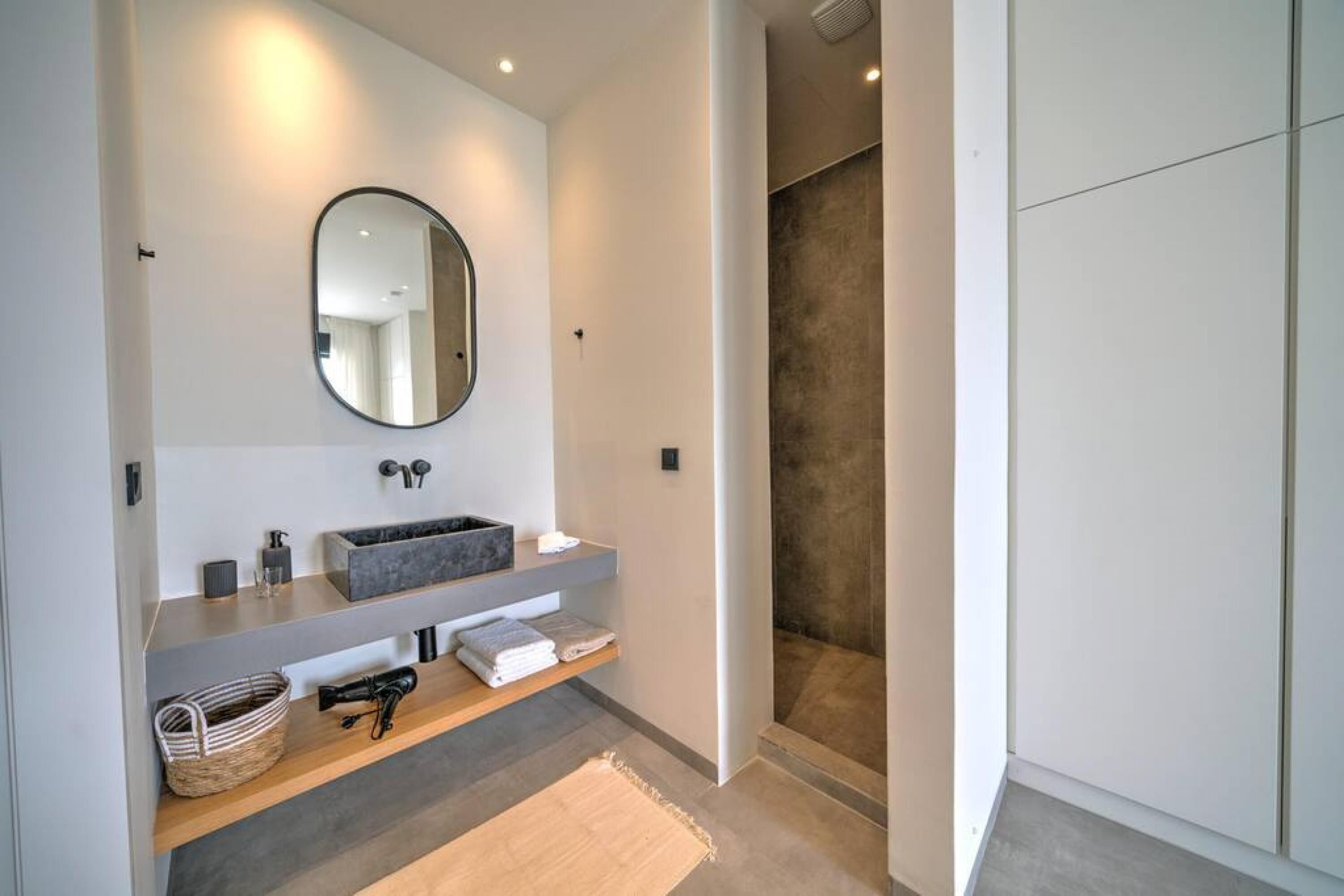 A modern bathroom with a grey sink, a round mirror, and a shower area.