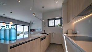 A modern kitchen with wooden cabinets, a built-in dishwasher, and pendant lighting. - Villa Chelidoni in Mariou (Agios Vasileios)