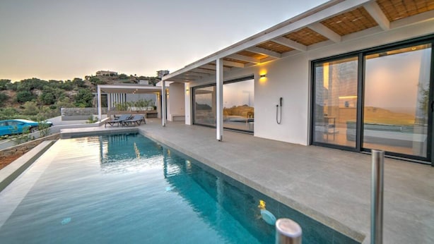 A modern poolside area with a clear pool, outdoor seating, and a view of the surrounding landscape. - Villa Chelidoni in Mariou (Agios Vasileios)