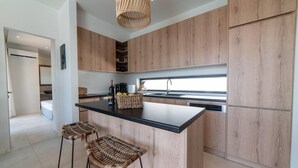 A modern kitchen with wooden cabinets, a black countertop, and two wicker bar stools. - Villa Mare in Mariou (Agios Vasileios)