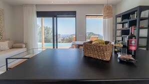 A modern kitchen with a large island, a dining area with a view, and a bookshelf with wine bottles. - Villa Mare in Mariou (Agios Vasileios)