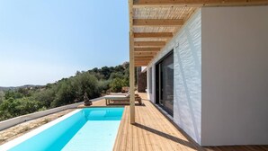 A modern outdoor swimming pool with a wooden deck, a stone statue, and a view of the surrounding landscape. - Villa Mare in Mariou (Agios Vasileios)