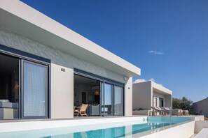 A modern building with a swimming pool, large sliding glass doors, and outdoor seating. - Villa Aragma in Mariou (Agios Vasileios)