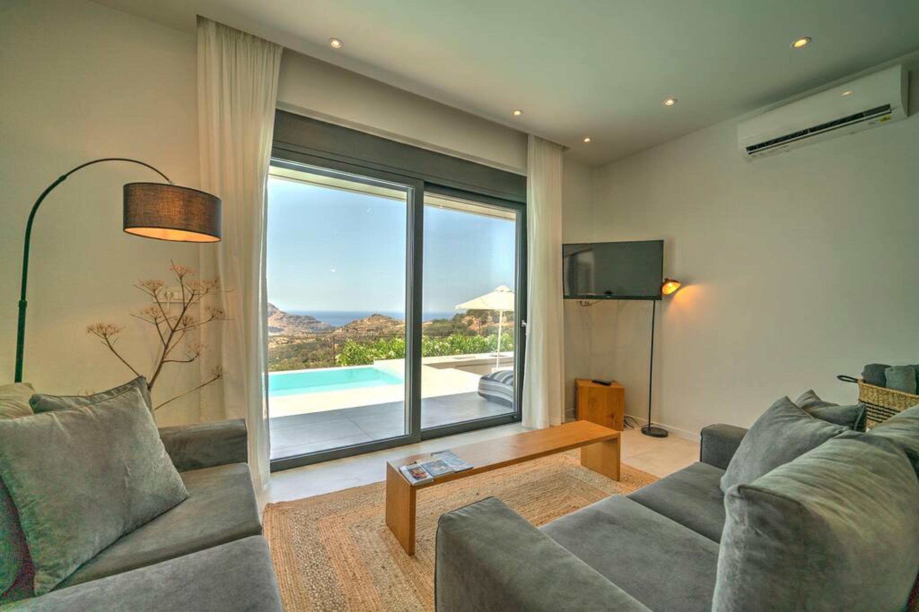 A modern living room with a large sliding glass door leading to a pool, a flat-screen TV, and a cozy seating area.