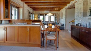 A spacious kitchen with wooden cabinets, a central island, and a dining area with chairs and a table. - Villa Helios in Foinikas (Agios Vasileios)