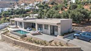 A modern house with a swimming pool, a car, and a view of a hillside with other houses. - Villa Oniriko in Mariou (Agios Vasileios)