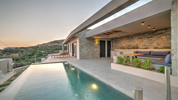 A modern outdoor pool area with a stone wall and seating. - Villa Oniriko in Mariou (Agios Vasileios)