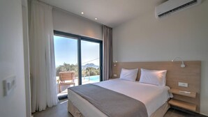 A modern hotel room with a large bed, a wooden headboard, a bedside table, and a view of the outdoors through a sliding glass door. - Villa Oniriko in Mariou (Agios Vasileios)