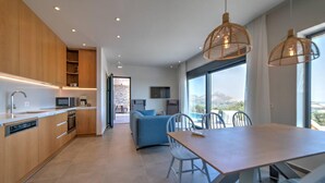 A modern kitchen with wooden cabinets, a dining area with a table and chairs, and a large window offering a view. - Villa Oniriko in Mariou (Agios Vasileios)