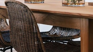 A wooden dining table with two glass vases containing white flowers, a wicker chair, a potted plant, and a microwave in the background. - Villa Petra in Plakias (Agios Vasileios)