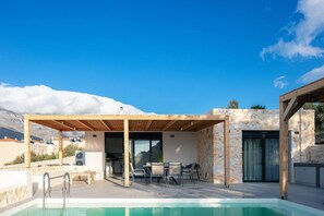 A rooftop pool area with a covered seating area, stone walls, and a view of the mountains.