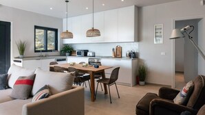 A modern kitchen with white cabinets, a dining area with a wooden table and chairs, and pendant lighting. - Villa Petra in Plakias (Agios Vasileios)