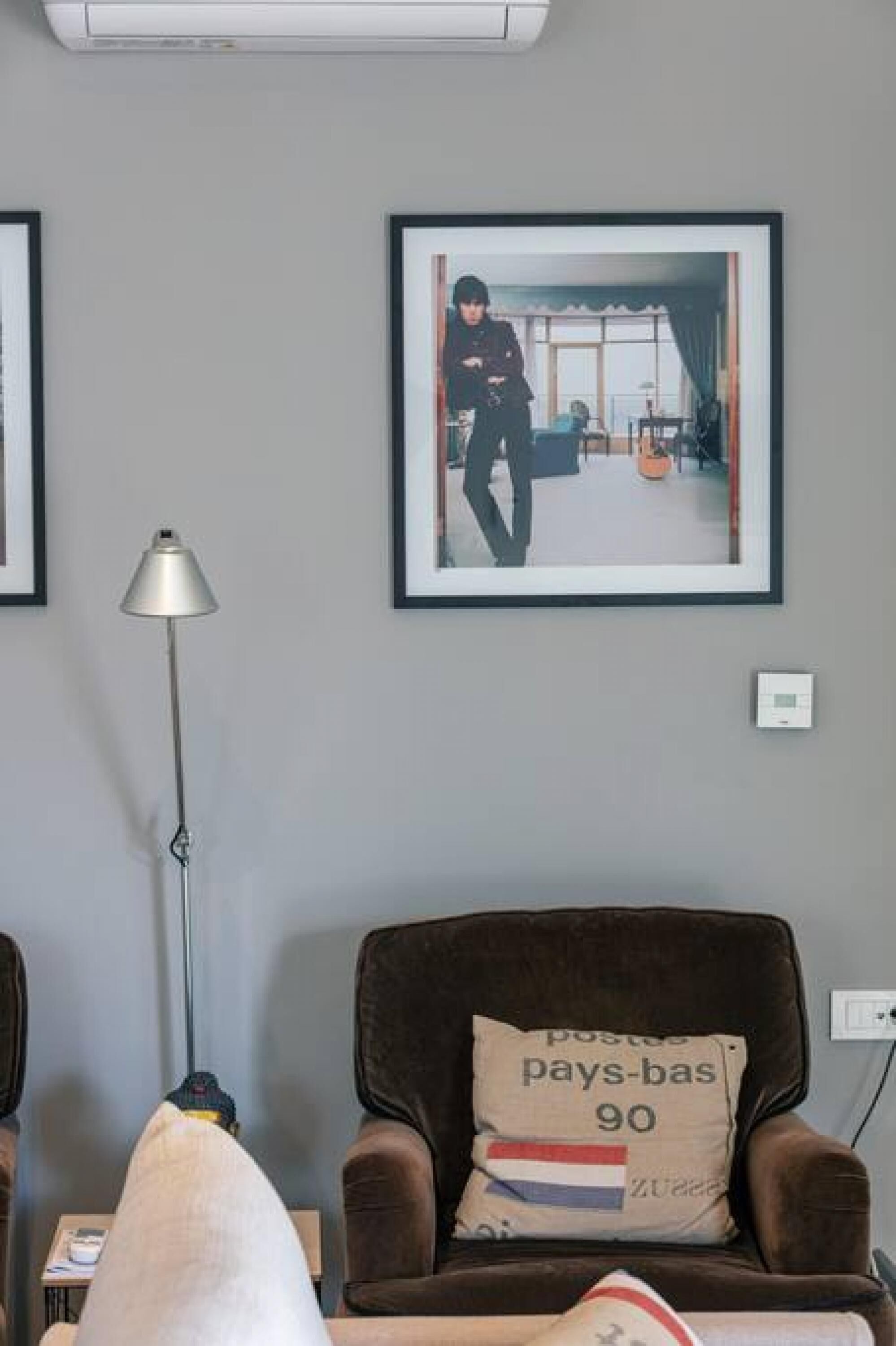 Una habitación con un sillón marrón, un cuadro en la pared, una lámpara de pie y un enchufe.