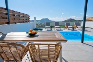 A rooftop terrace with a pool, wicker chairs, a table with fruit, and a view of the landscape. - Villa Iris in Mariou (Agios Vasileios)