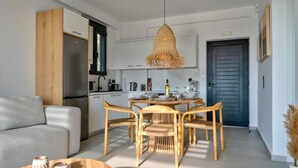 A modern kitchen with white cabinets, a wooden dining table with chairs, and a hanging light fixture. - Villa Saturday in Foinikas (Agios Vasileios)
