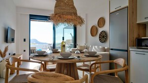 A modern kitchen with a round dining table, wooden chairs, and a hanging light fixture. - Villa Saturday in Foinikas (Agios Vasileios)