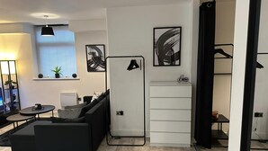 Ett modernt vardagsrum med en svart soffa, ett litet runt bord, ett vitt skåp och ett konstverk med svart ram på väggen.