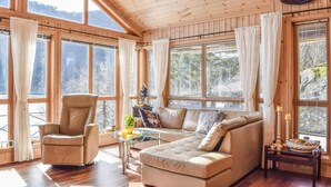 A cozy living room with a leather armchair, a sofa, and a glass coffee table. Large windows offer views of a snowy landscape. - 4 bedroom cozy home in Farsund (Farsund)