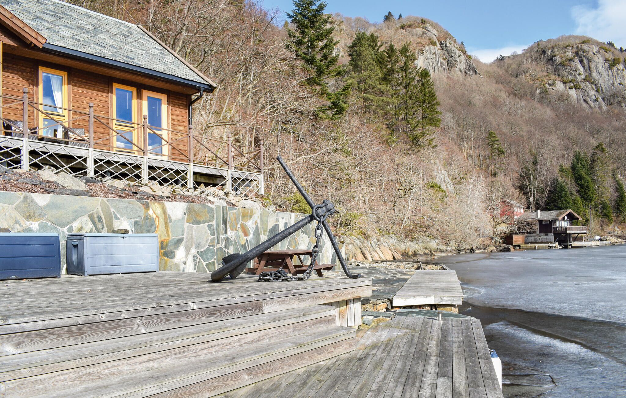 A wooden cabin with a stone wall and a dock extending into a frozen river.