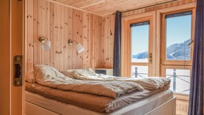 A wooden-paneled room with a bed, two windows, and a view of a snowy landscape. - 4 bedroom cozy home in Farsund (Farsund)