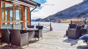 A wooden deck with wicker furniture overlooking a body of water and hills. - 4 bedroom cozy home in Farsund (Farsund)