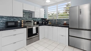 A modern kitchen with white cabinets, a stainless steel refrigerator, a microwave, an oven, and a sink. - Zana del Mar | Steps from the Beach (Humacao)