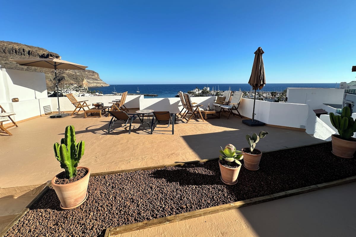 A rooftop terrace with outdoor seating, potted plants, and a view of the sea.