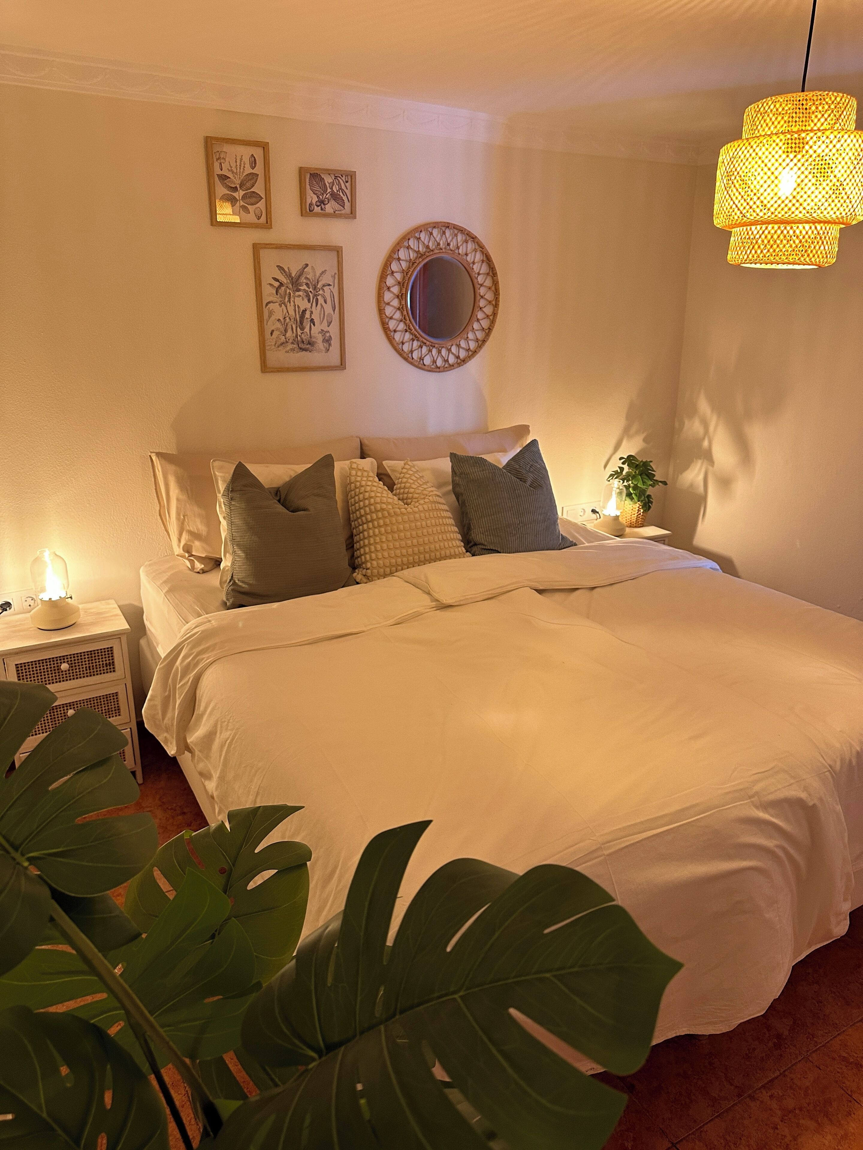 A neatly made bed with white linens, a bedside table with a lamp, and a wall-mounted mirror.