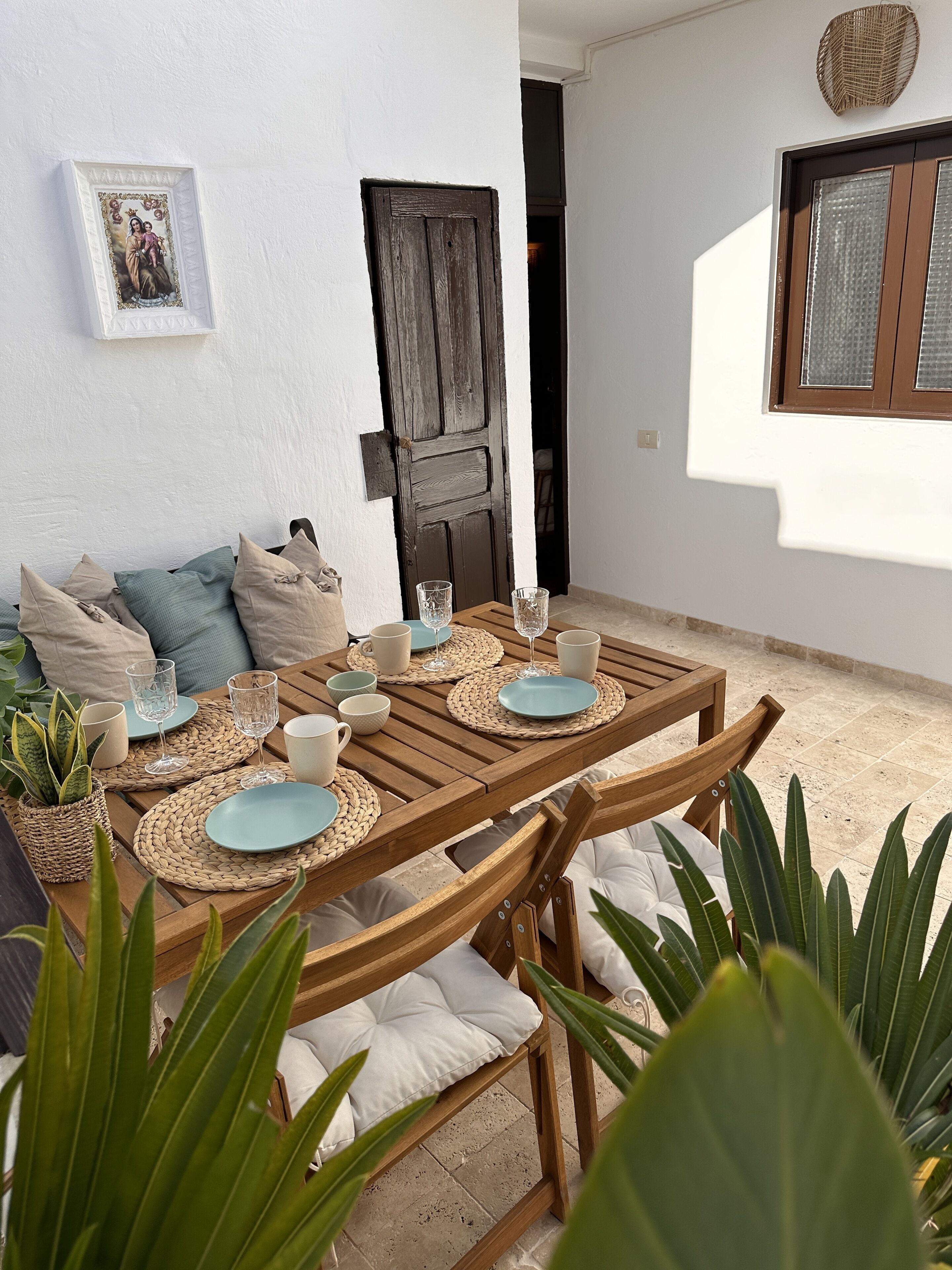 A wooden table set with plates, cups, and glasses, surrounded by cushioned chairs and a woven placemat.