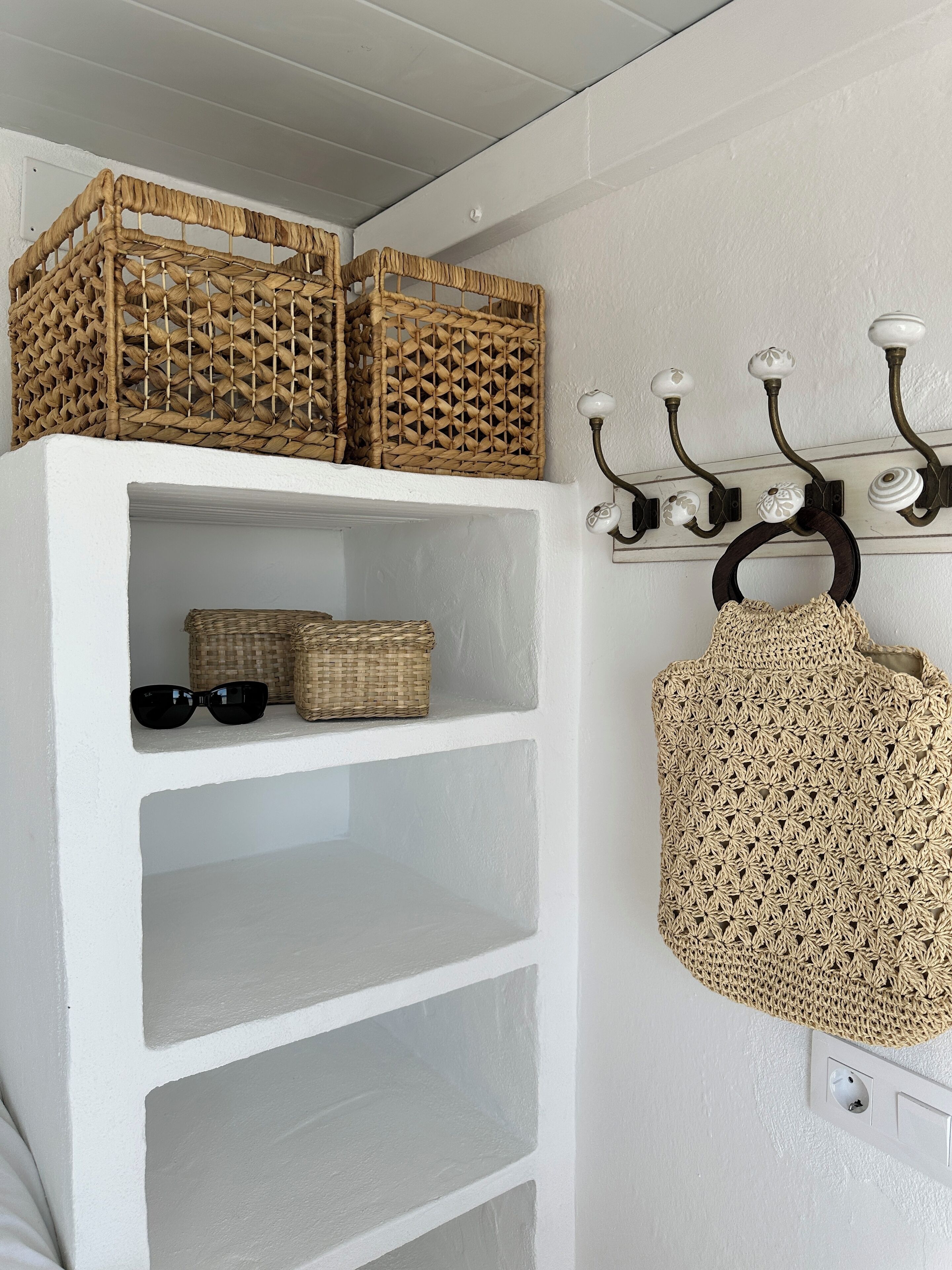 Une étagère blanche avec des paniers en osier et un sac en crochet.