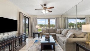 A spacious living room with a large flat-screen TV, a ceiling fan, a sectional sofa, and a coffee table. - Edgewater Golf Villas 1714 | Family-Friendly Community, Beach Access, Lagoon-Style Pool (Panama City Beach)