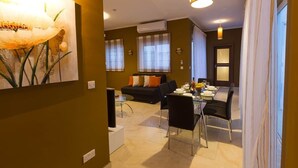 A modern living room with a dining area, featuring a sofa, a dining table set for four, and a large painting on the wall.