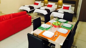 Ein Hotelzimmer mit zwei Einzelbetten, einem roten Sofa, einem Esstisch für vier Personen und Bildern an den Wänden.