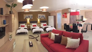 Ein Hotelzimmer mit rotem Sofa, mehreren Betten, einer Essecke und einer Küchenzeile.